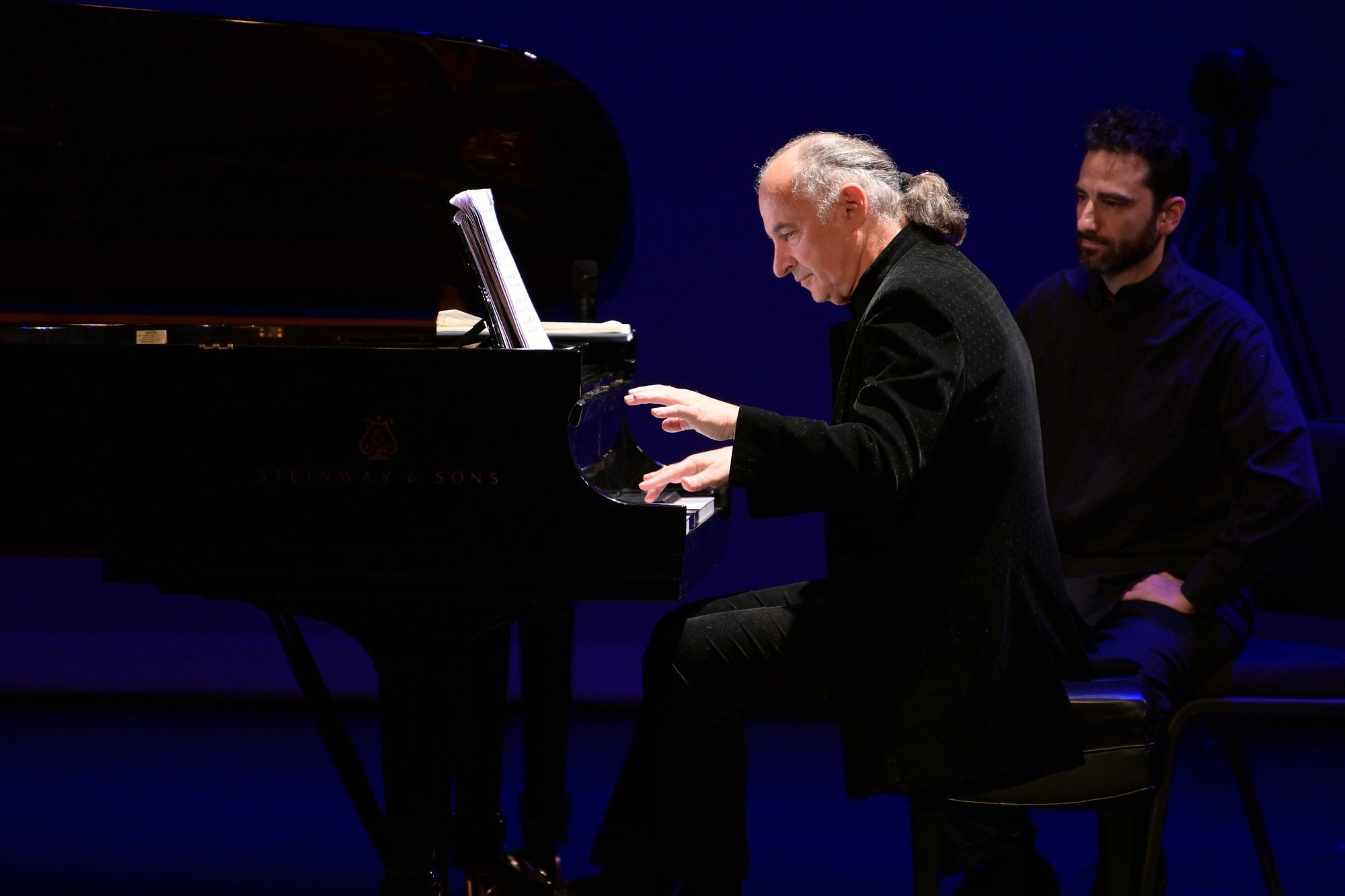 A pianist at the keyboard, with a companion seated beside him
